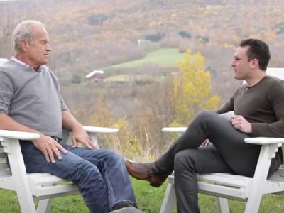 Kelsey Grammer and Graham Besinger are out in the field, sitting in a chair, talking face to face with each other. 